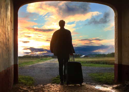 Zdjęcie mężczyzny z walizką odchodzącego w stronę zachodzącego słońca